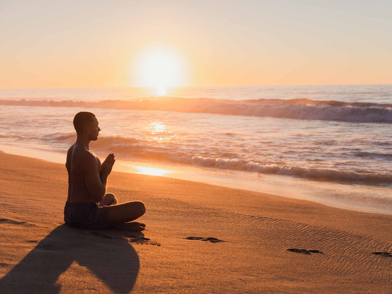 Persona meditando sentada en la arena frente al amanecer sobre el mar