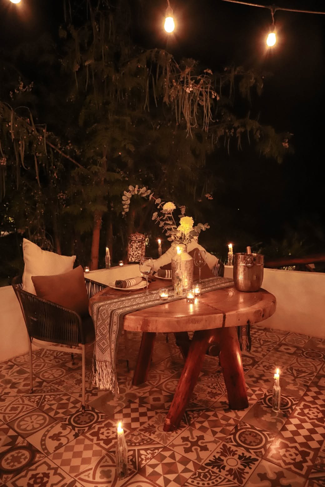 Mesa redonda montada con velas y cubeta de hielo bajo las luces del jardín