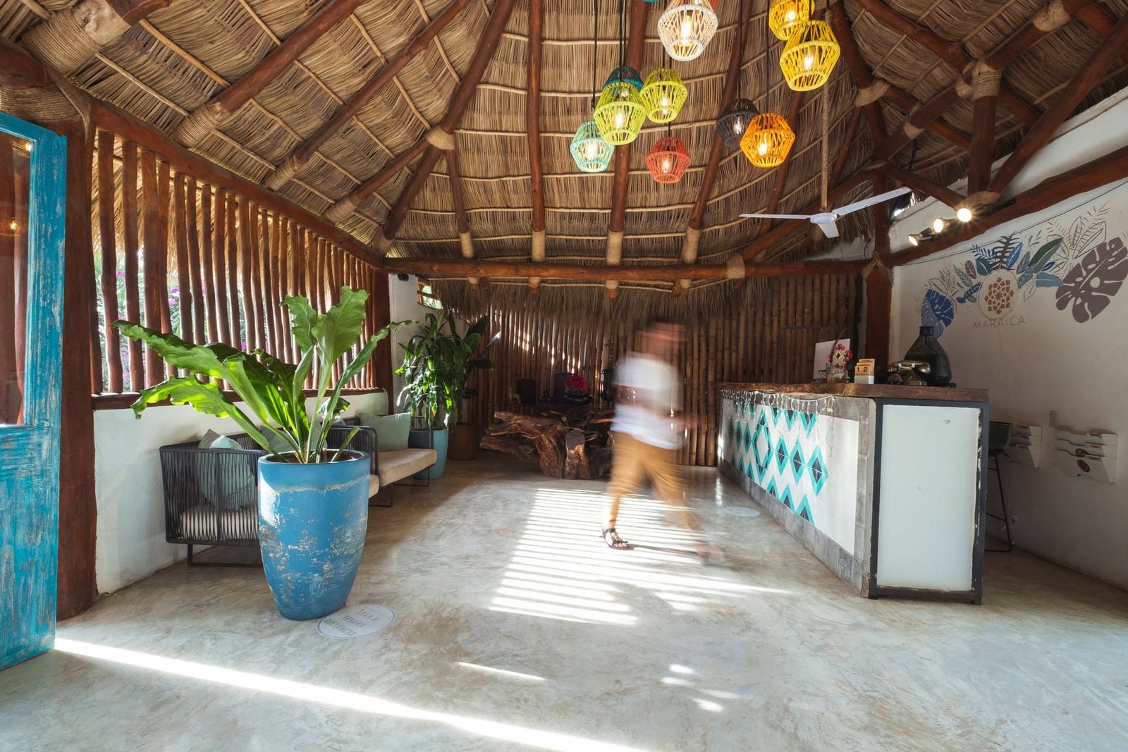 Recepción bajo techo de palapa con lámparas colgantes y una maceta azul