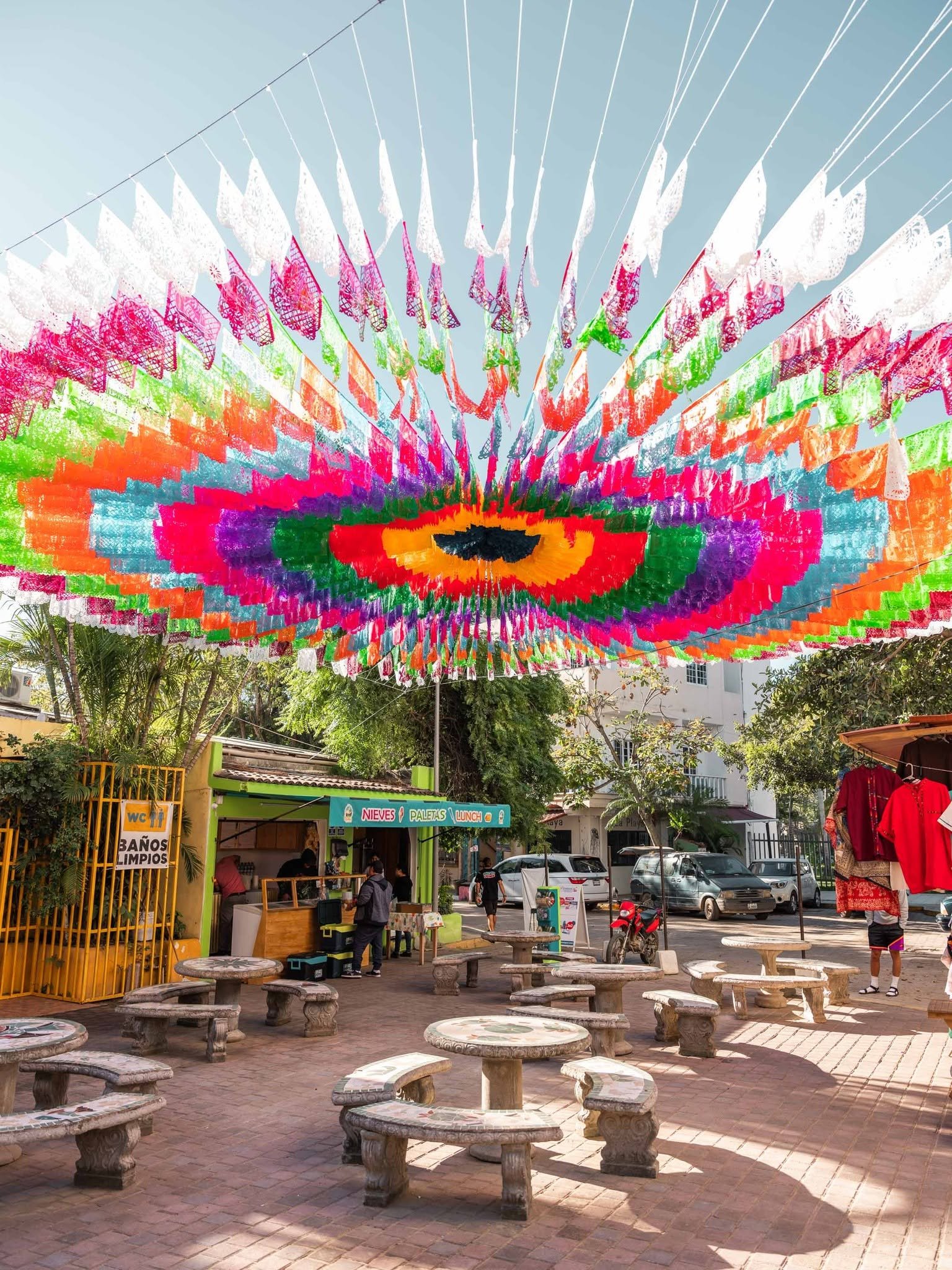 Plaza del pueblo cubierta de papel picado de colores sobre mesas de piedra
