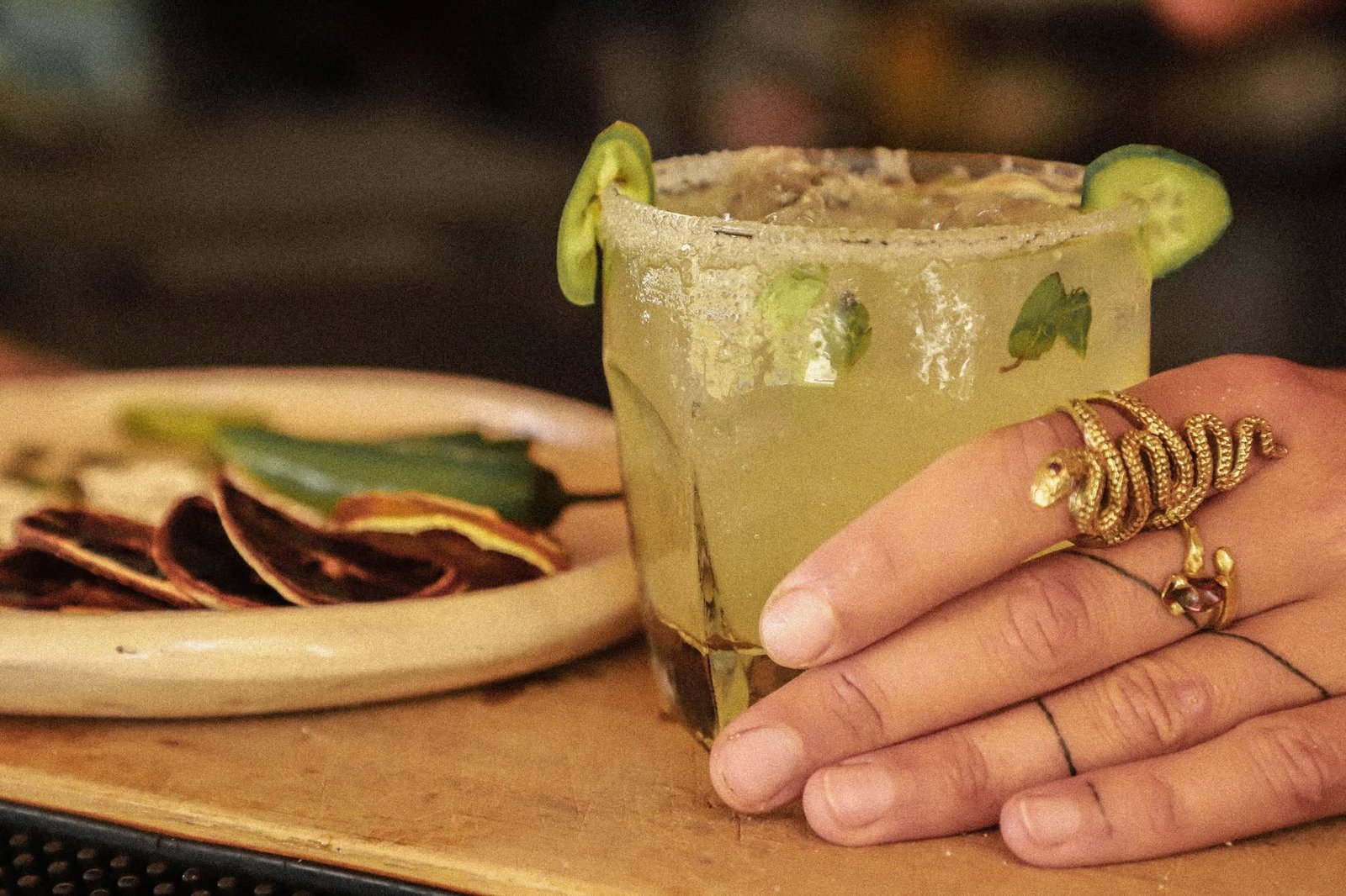 Margarita con sal y pepino servida junto a un plato de tostadas en la barra