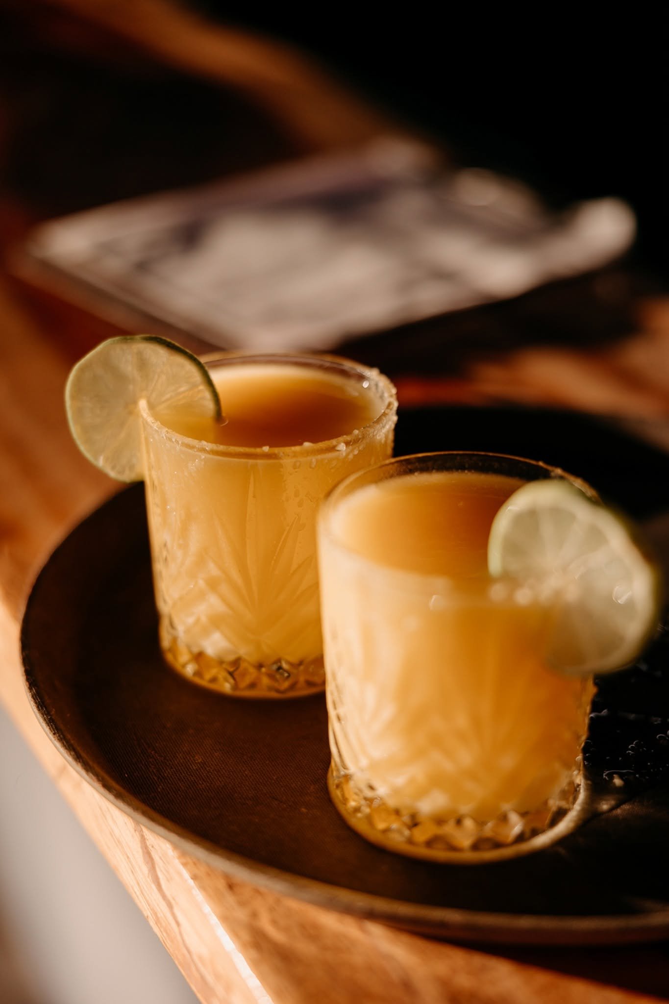 Dos cócteles de mezcal con lima servidos en una charola de madera