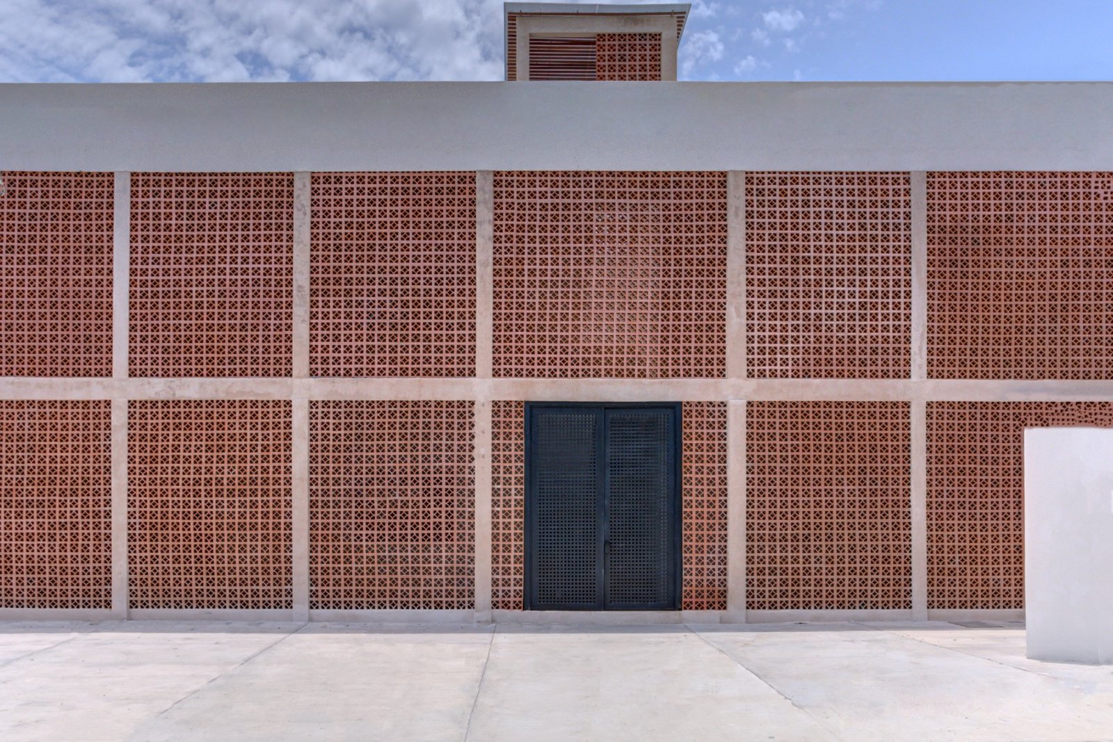 Fachada de Mamica La Cruz: muro de celosía de barro con la puerta de acceso