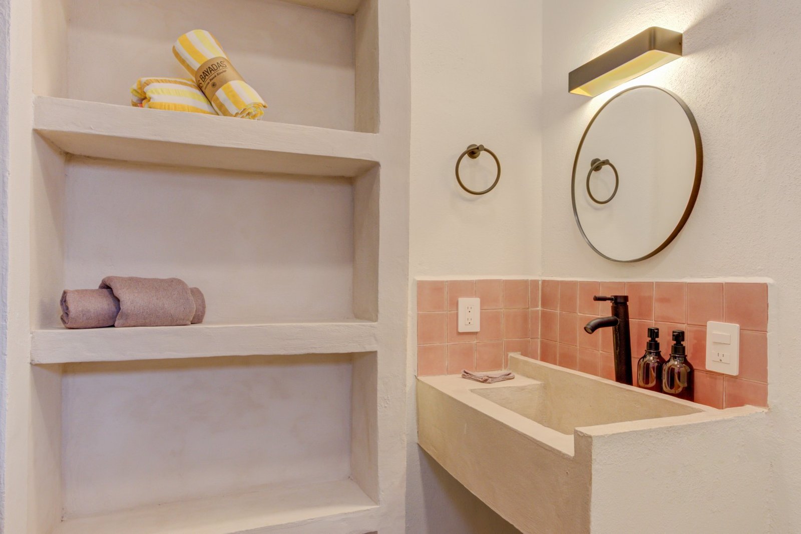 Baño con lavabo de obra, espejo redondo y amenidades