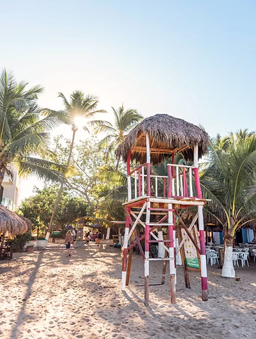 Torre de salvavidas de rayas rosas en la playa de San Pancho, entre palmeras