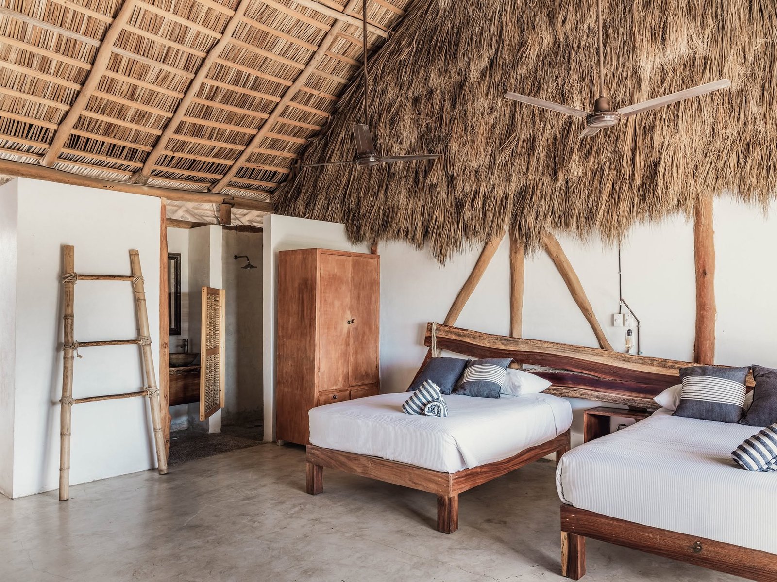 Habitación con dos camas, muros encalados, escalera de bambú y techo de palma