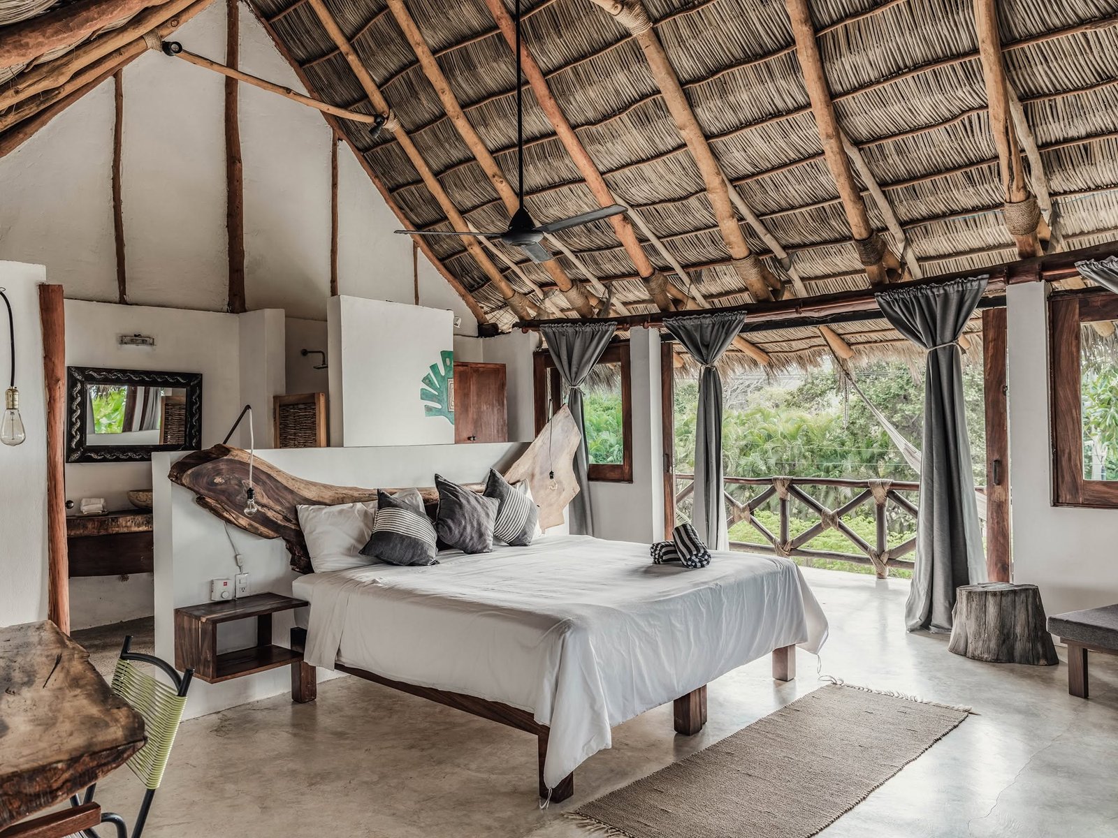 Habitación con cama king, techo de palapa a doble altura y cortinas abiertas al jardín